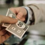 Jak negocjować z platformami warunki wyróżnień promocji i lepszej ekspozycji gry Zbliżenie na dłonie wymieniające banknoty Monopoly jako transakcję finansową